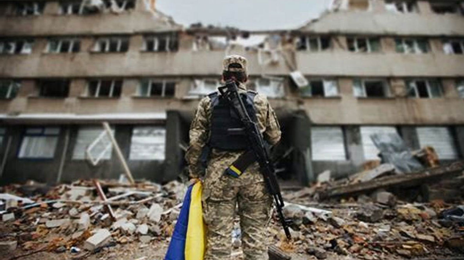 جندي يحمل علم أوكرانيا ويقف أمام مبنى مدمّر (فرانس برس)