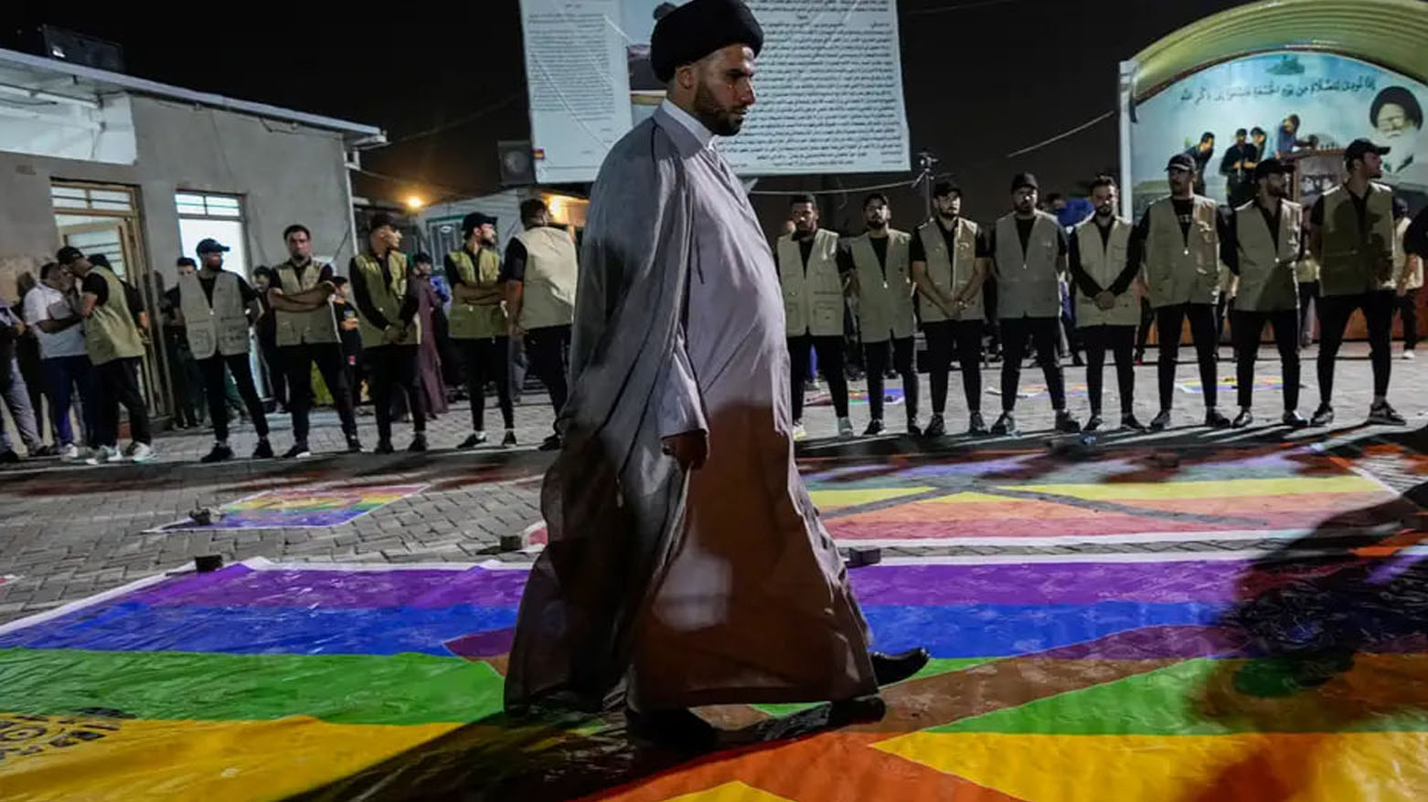 روحانی عراقی در حال پا گذاشتن بر پرچم رنگین کمان که نماد دگرباشان جنسی است