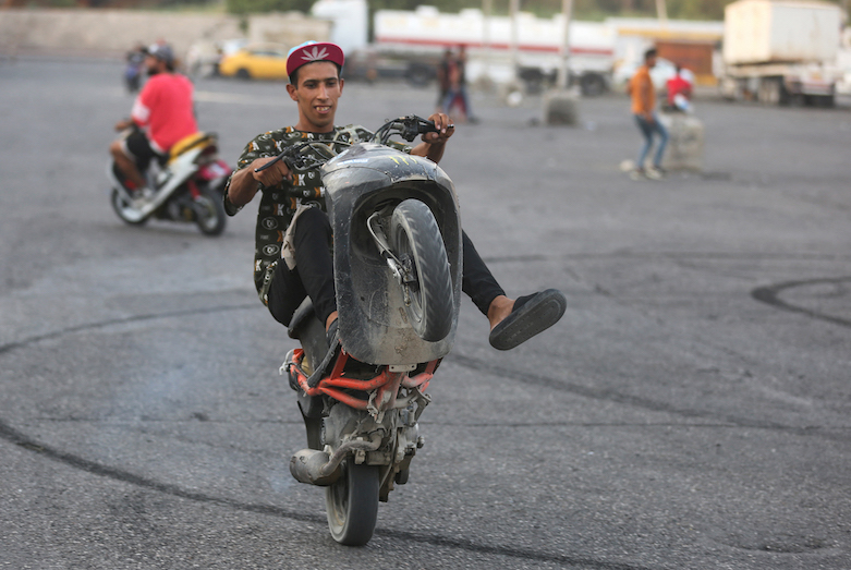 Iraqi youths perform stunts on their scooters in the Jadriya district of Baghdad, August 6, 2021. (Photo: Ahmad Al-Rubaye/AFP)