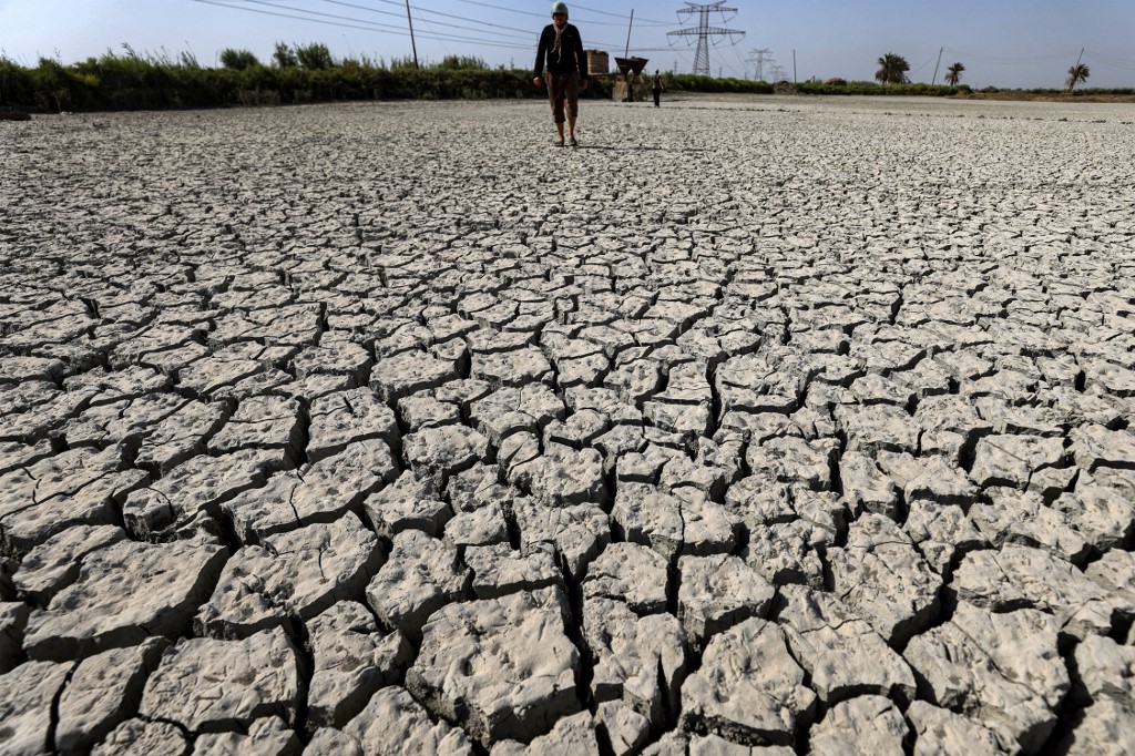 A man walks on cracked mud covering the surface of a dry fish farm in the village of Albu Mustafa in Hilla July 6, 2023. (Photo: Ahmad Al-Rubaye/AFP)