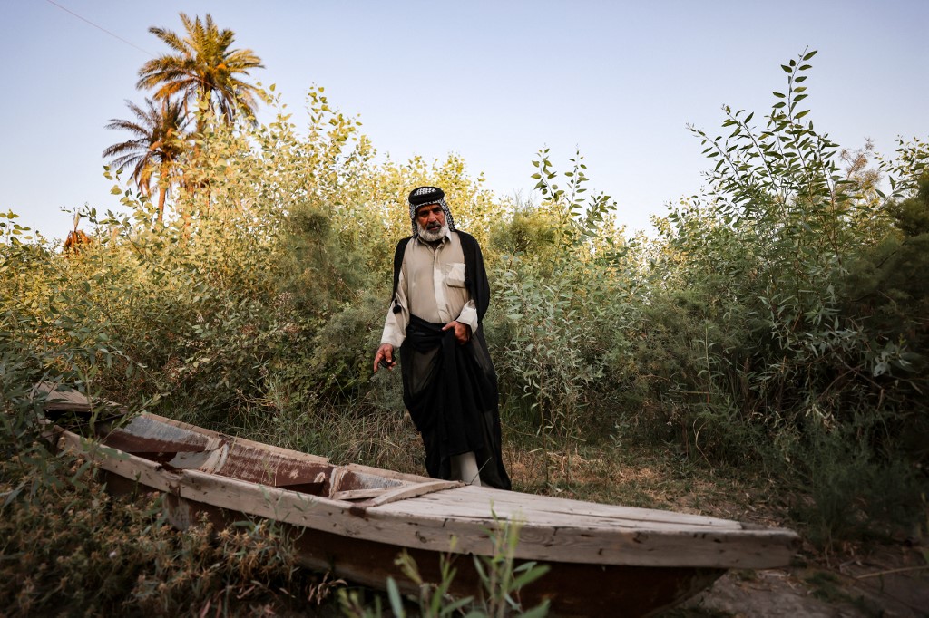 A man stands next to his fishing boat, abandoned on the banks of a branch of the Euphrates River in the town of Al-Hamza near the city of Hilla, July 6, 2023. (Photo: Ahmad Al-Rubaye/AFP)