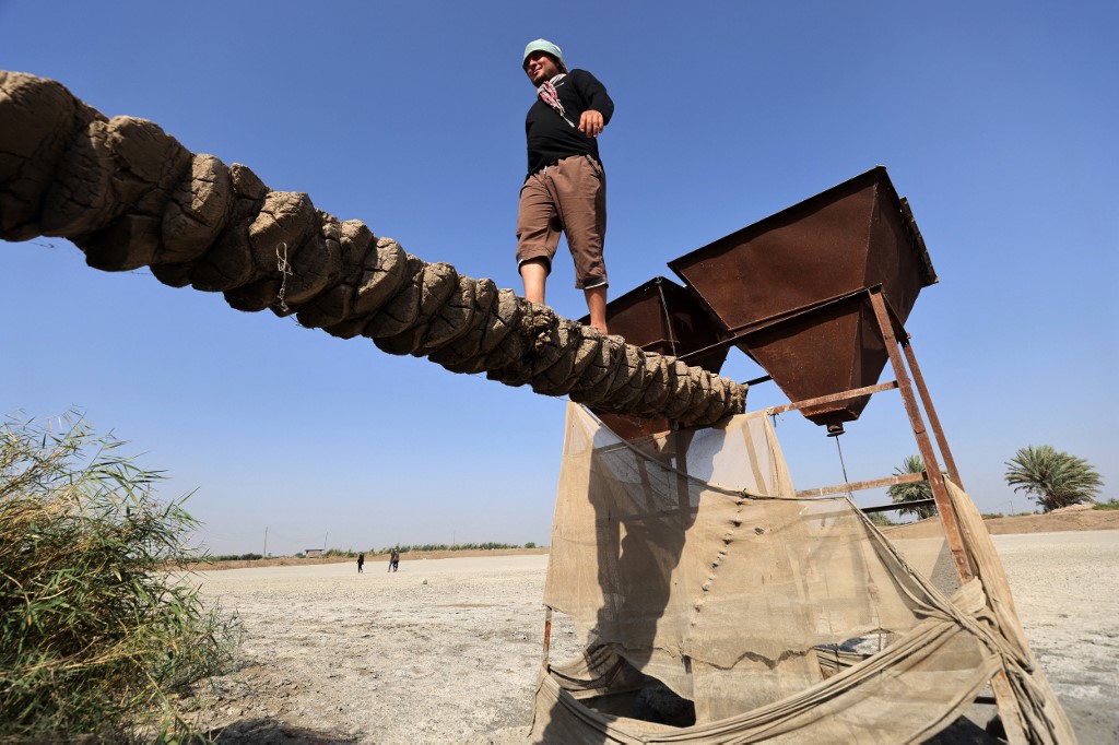 A man walks on a makeshift bridge connecting dry land to a fish feeding deice, standing on what is now a dry fish farm in the village of Albu Mustafa in Hilla, July 6, 2023. (Photo: Ahmad Al-Rubaye/AFP)