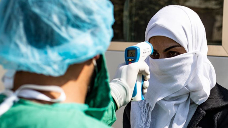 A healthcare worker checks the temperature of a woman arriving by bus to Rojava from the Kurdistan Region to test for coronavirus, Feb. 26, 2020 (Photo: AFP/Delil Souleiman)
