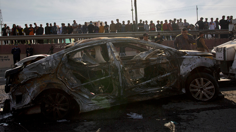 A picture shows bystanders near a destroyed car in the southern Iraqi city of Basra after at least four civilians were killed and four more wounded in a motorcycle bombing near a hospital, Dec. 7, 2021. (Photo: Hussein Faleh/AFP)