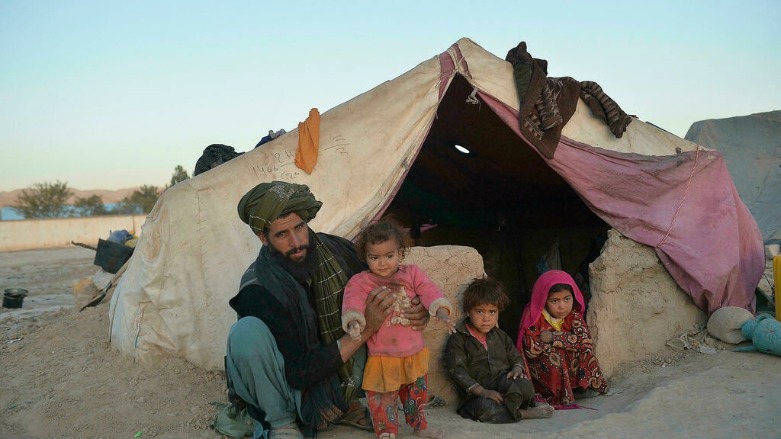 طفلتان تجلسان مع والدهما أمام خيمة في مخيم للنازحين في قلعة نو في إقليم باغديس في أفغانستان، في ظل تفاقم الأزمة الإنسانية بالبلاد - الصورة لفرانس 24