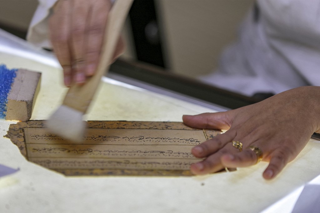 A conservator brushes a manuscript fragment undergoing restoration at the Iraqi Manuscript House's resoration lab in Iraq's capital Baghdad, Dec. 6, 2022. (Photo: Sabah Arar/AFP)