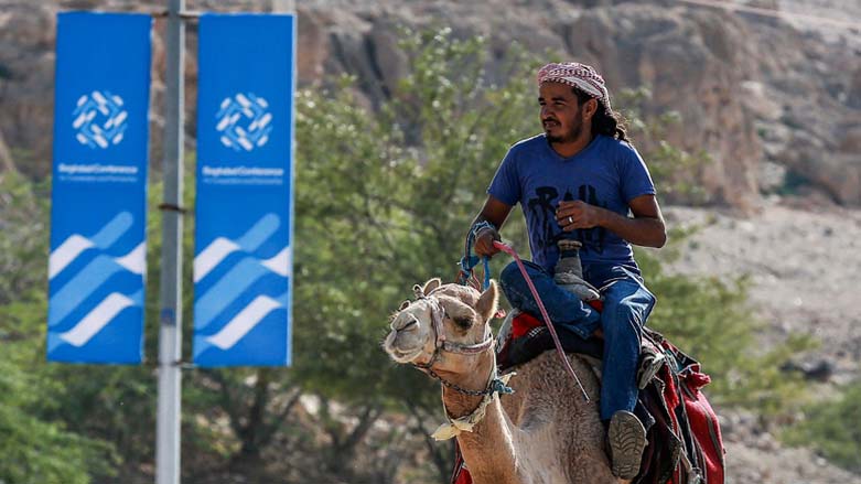 A man rides a camel along a road past signs bearing the name and logo of the "Baghdad Conference for Cooperation and Partnership", Dec. 19, 2022. (Photo: Khalil Mazraawi/AFP)
