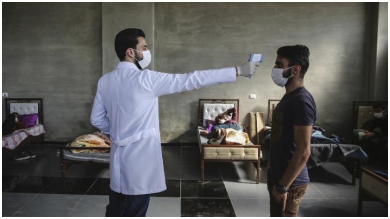 A medic checks the temperature of a man inside a health isolation center on the Syrian-Turkish borders. (Photo: AP/Anas Alkharboutli)