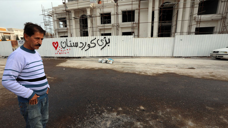 A man stands on February 16, 2021 near a fence with graffiti reading in Kurdish "long live Kurdistan", at the scene of a rocket attack targeting Arbil the previous night, Feb. 16, 2021. (Photo: Safin Hamed / AFP)