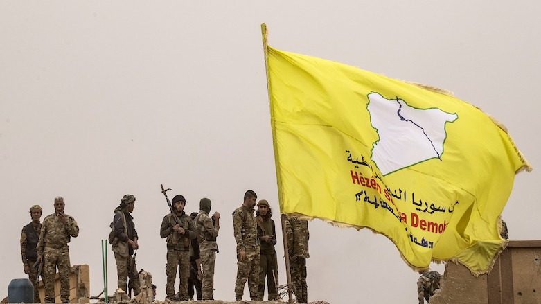 Syrian Democratic Forces fighters stand on a roof next to their flag in the village of Baghouz, Deir al-Zor province, Syria, March 24, 2019 (Delil Soleiman / AFP).