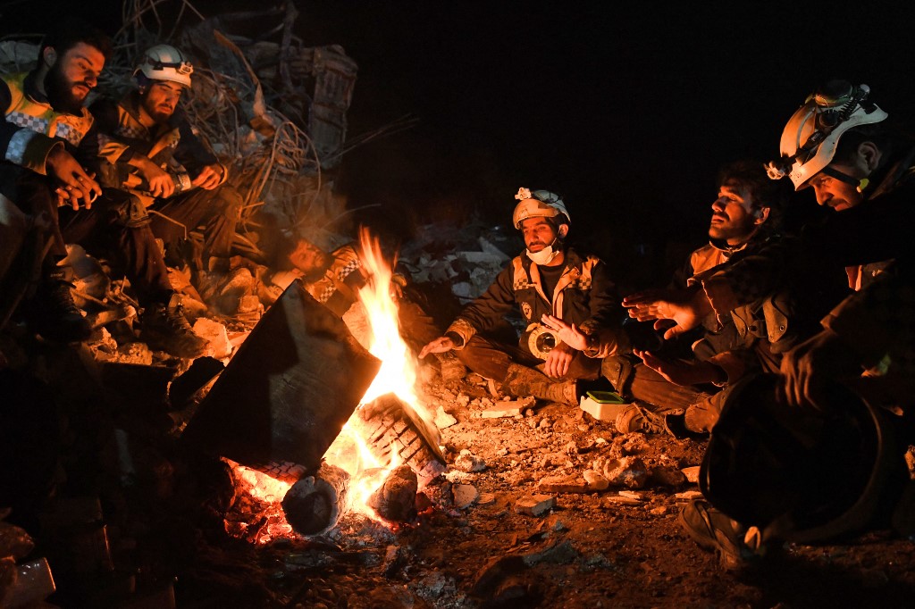 Members of the Syrian civil defence, known as the White Helmets, warm themselves by a fire next to the rubble of a collapsed building late, Feb. 7, 2023. (Photo: Rami Al-Sayed/AFP)