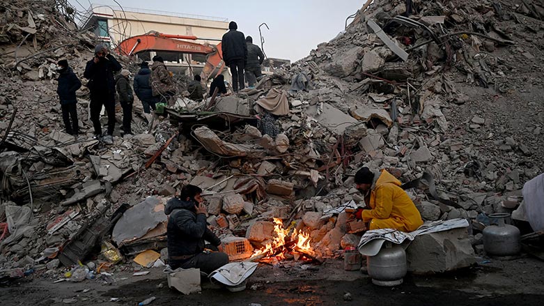 Relatives warm up around a fire in front of rubble of collapsed buildings as rescue teams continue to search victims and survivors, on February 12, 2023 (Photo: Ozan Kose/ AFP)
