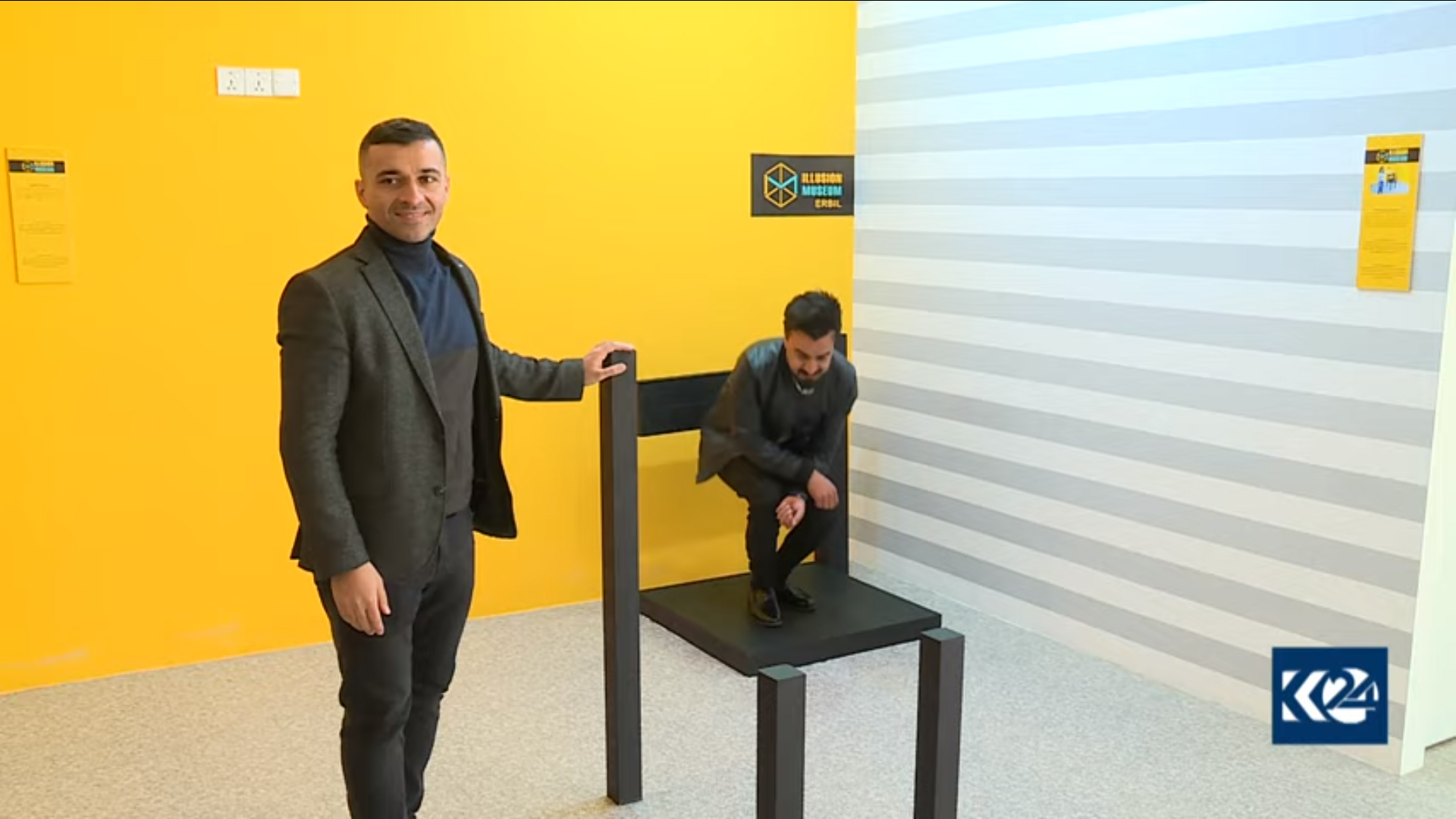 A man is seen standing on a chair while another one is sitting behind. (Photo: Kurdistan 24)