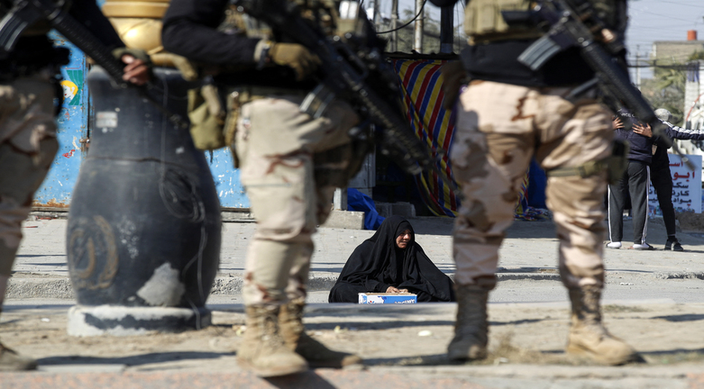A woman sits on the ground as Iraqi soldiers man a checkpoint in the the capital Baghdad on January 28, 2022, following a reported rocket attack on the country's airport, Jan. 28, 2022. (Photo:  Ahmad al-Rubaye/AFP)