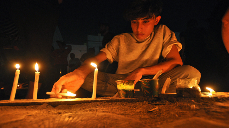 A young man light up candles for a vigil in mourning for the victims of a fire that swept through a COVID-19 coronavirus isolation, July 14, 2021. (Photo: Asaad Niazi/AFP)