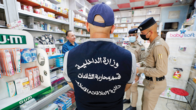 A member of Iraq's Interior Ministry's anti-"fake news" team, accompanied by policemen, speak to a pharmacist in the capital Baghdad, May 20, 2021. (Photo: Ahmad Al-Rubaye/AFP)