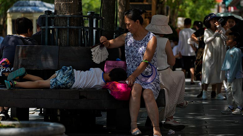 A woman uses a fan to cool a child as they sit on a bench at Qianmen pedestrian shopping street on a hot day in Beijing, June 29, 2023. (Photo: AP/Andy Wong)
