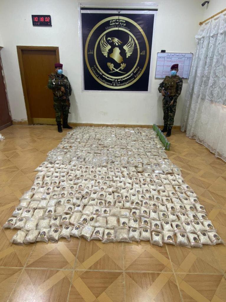 Confiscated narcotic pills on display, with two security guards. (Photo: Iraqi Security Media Cell)
