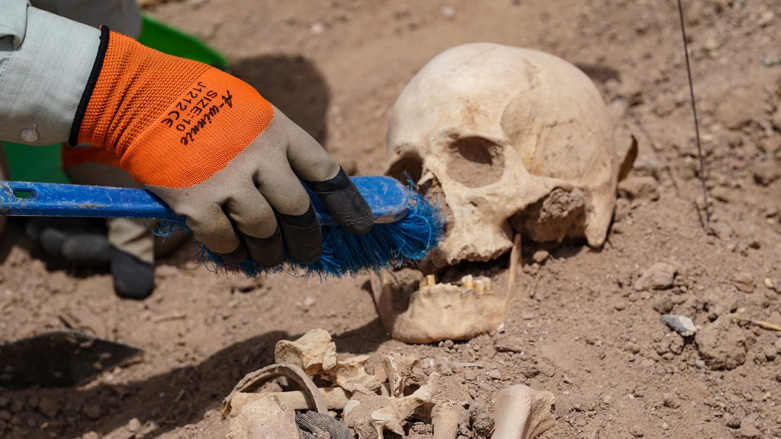 A forensics expert uses a brush to exhume a skull at the site of a mass grave, discovered by chance when property developers wanted to prepare the land for construction, in the central city of Najaf, May 18, 2022. (Photo: Qassem Al-Kaabi/AF