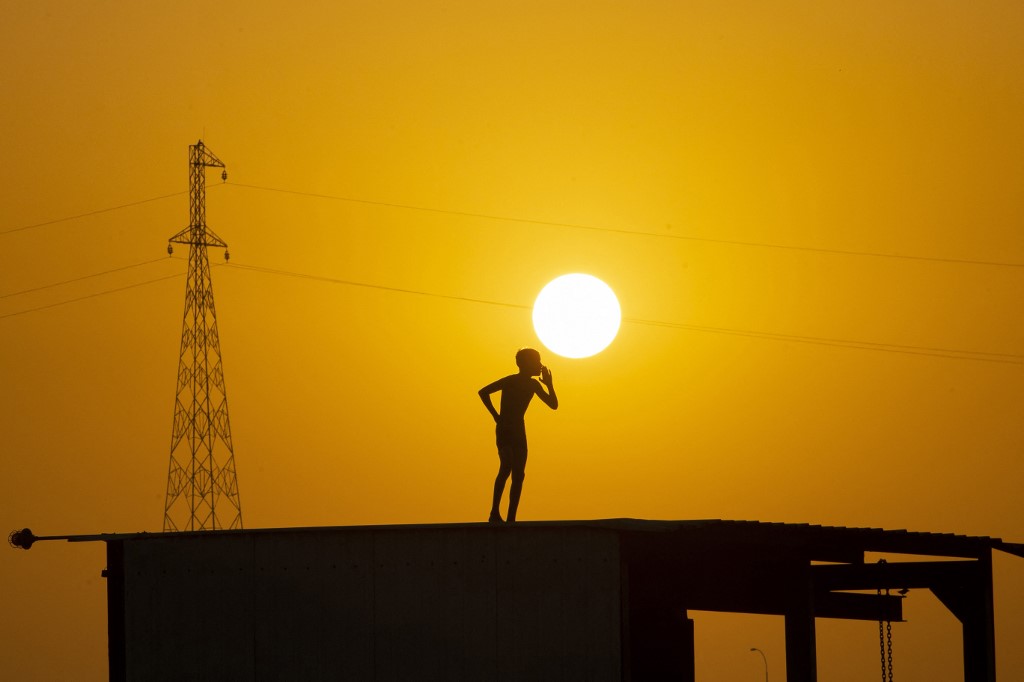 A boy prepares to jump off the roof of a structure to cool off in the waters of the Shatt al-Arab waterway, June 18, 2022. (Photo: Hussein Faleh/AFP)