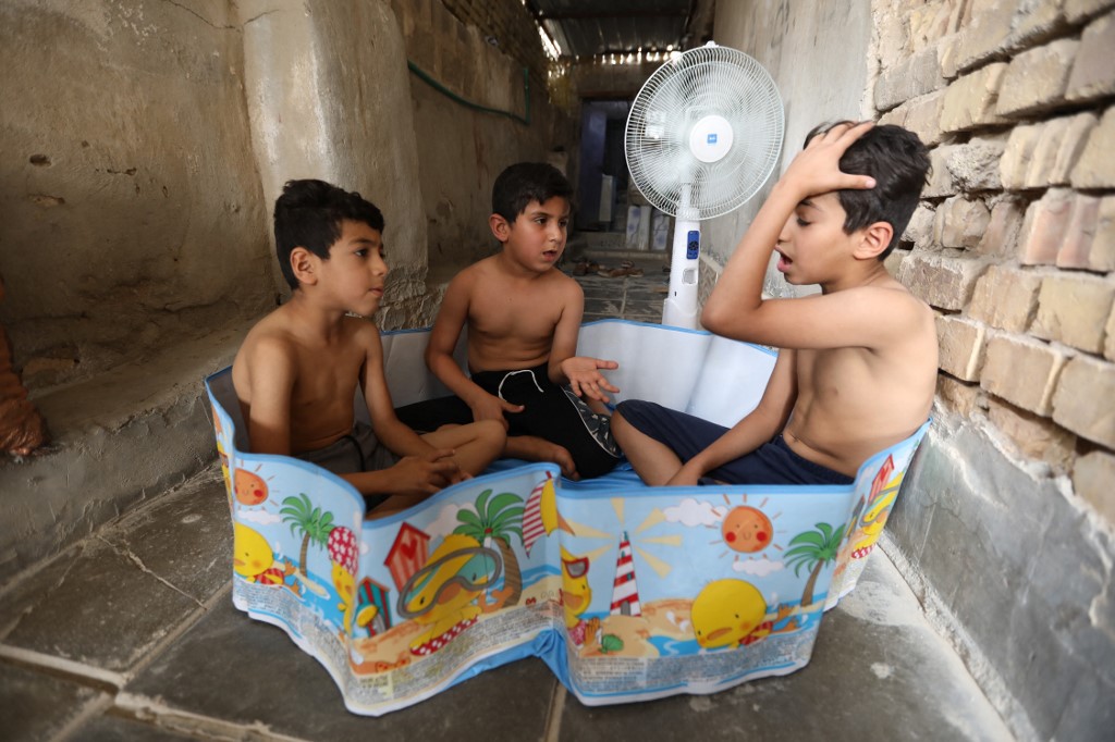 The sons of Nateq Khafaji sit in an empty pool next to a fan outside their home in the city of Nasiriyah in Iraq's southern Dhi Qar province, June 10, 2022. (Photo: Asaad Niazi/AFP)