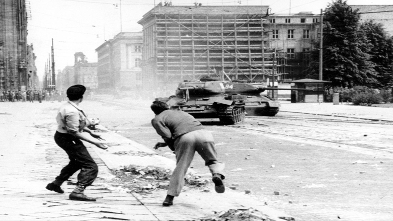 وێنەیەکی ئەرشیفی خۆپیشاندەران لە بەرلینی ڕۆژهەڵات لە 17ی حوزەیرانی 1953 بەرد لە&nbsp; تانکێکی سۆڤیەت دەگرن.