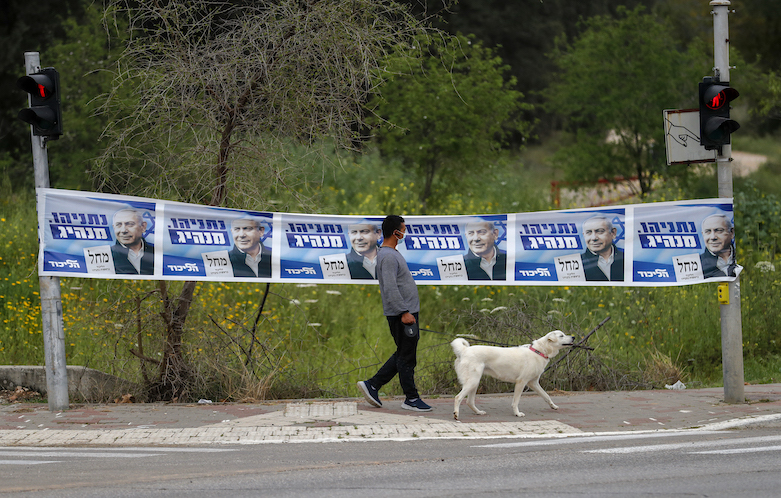 A man walks his dog past electoral posters for Israeli Prime Minister and candidate Benjamin Netanyahu in the Arab city of Kfar Qassem in central Israel, on March 22, 2021. (Photo: Ahmad Gharabli/AFP)