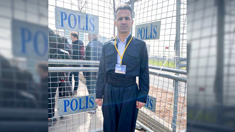 Hasan Kosen, Kurdistan 24's correspondent to Diyarbakir, poses for a photo in front of a Turkish police fence after he was banned from covering Newroz celebrations because of his traditional Kurdish outfit, Mar. 21, 2022. (Photo: Kurdistan