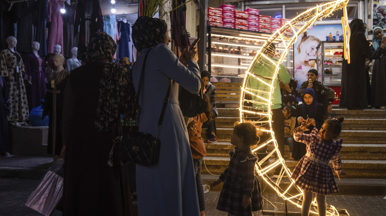یک زن فلسطینی در آغاز ماه مبارک رمضان در کمپ آوارگان جبلیه، شمال نوار غزه، از دخترش در کنار هلال ماه تزئینی در بازار عکس می‌گیرد _ عکس؛ آسوشیتد پرس