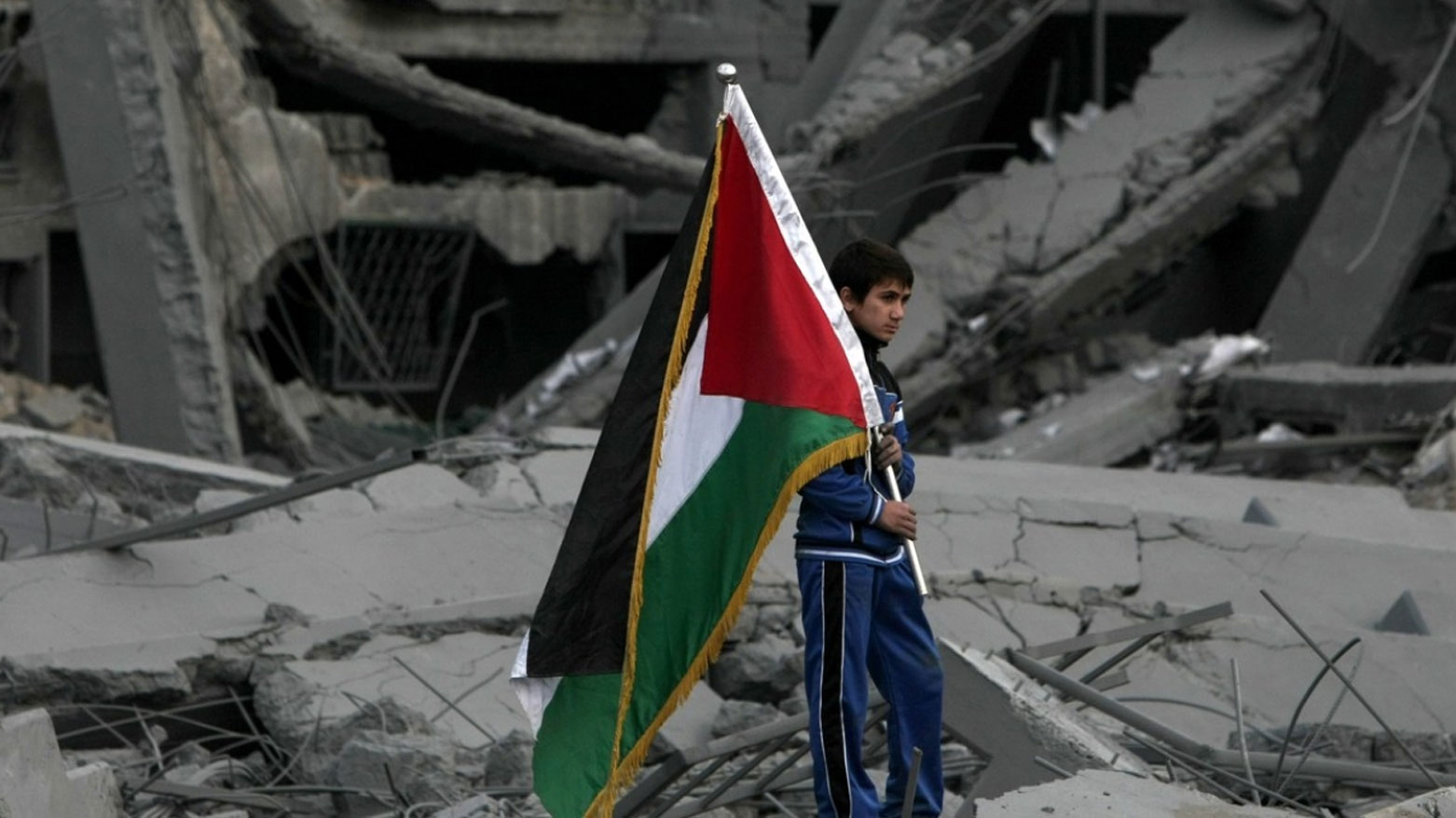 طفلٌ يقف على الأنقاض حاملاً العلم الفلسطيني