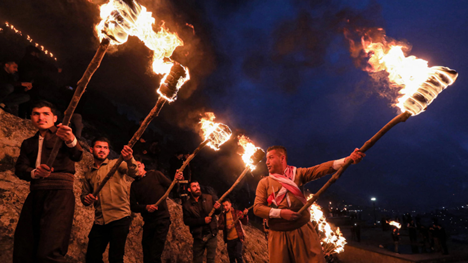 A number of men hold lit torches as they climb on a mountain in the Kurdistan Region Akre town on the eve of Kurdish New Year Newroz, March 20, 2022. (Photo: Safin Hamed/AFP)