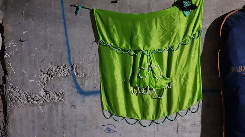 A colorful green fabric depicting the Yezidi temple at Lalish adorns a wall in a family’s makeshift home in Erbil, May 2021. (Photo: Wladimir van Wilgenburg)