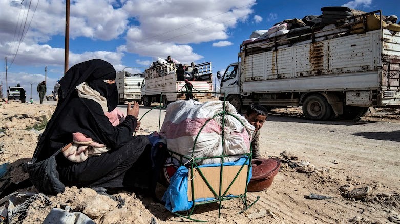 A Syrian woman and her child sit by their belongings awaiting departure as another group of families is released from the Kurdish-run al-Hol camp outside the northern Syrian city of Hasakah, March 18, 2021. (Photo: AFP/Delil Souleiman)