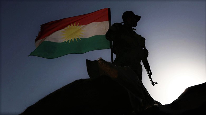 A Peshmerga fighter stands on guard next to the flag of Kurdistan. (Photo: Archive)