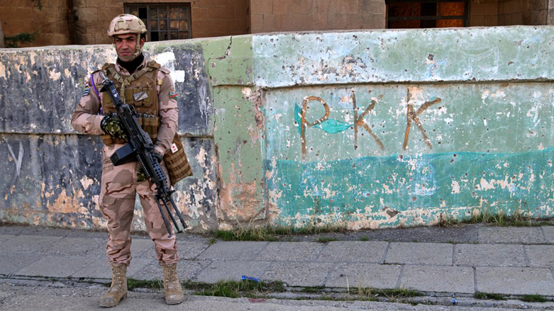 An Iraqi soldier standing guard by a wall with the acronym 'PKK' inscribed on it in Sinjar (Photo: AP)
