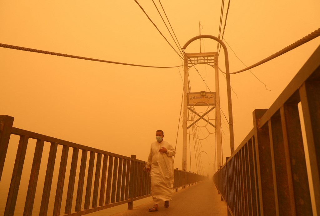 A man walks along a pedestrian bridge across the Euphrates river amidst a heavy dust storm in the city of Nasiriyah in Iraq's southern Dhi Qar province, May 23, 2022. (Photo: Asaad Niazi/AFP)