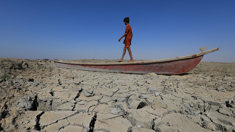 A boy walks on a boat left lying on the dried-up bed of a section of Iraq's receding southern marshes of Chibayish in Dhi Qar province, June 28, 2022. (Photo: Asaad Niazi/AFP)