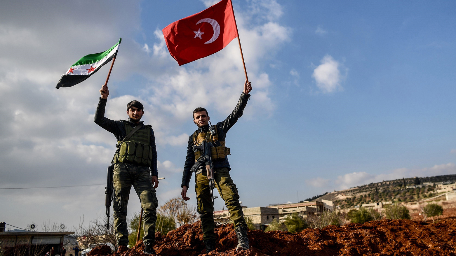 Turkish-backed Syrian rebel fighters hold a Turkish national flag and a Free Syrian Army flag at a checkpoint in Azaz on a road leading to Afrin (Photo: AFP)
