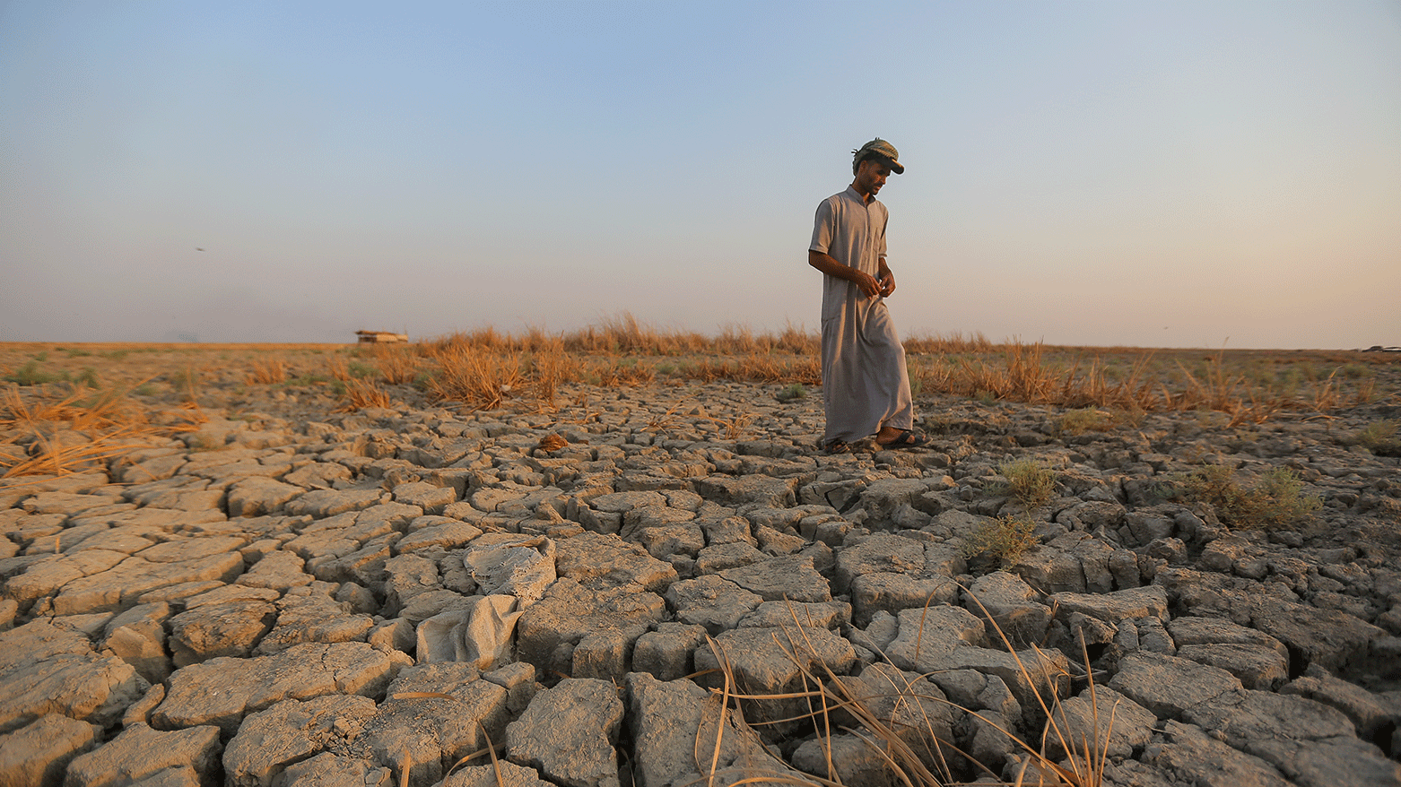 A fisherman walks across a dry patch of land in the marshes in Dhi Qar province, Iraq, Sept. 2, 2022. (Photo: Anmar Khalil/ AP)