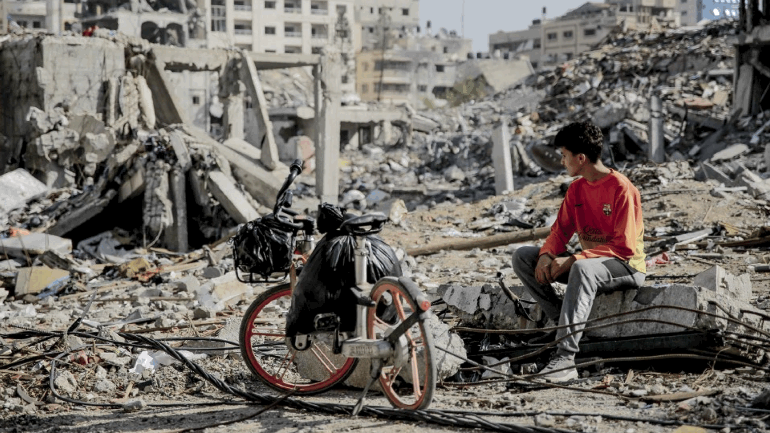 A Palestinian youth sits next to his bicycle amid the rubble of destroyed buildings in Gaza City (Photo: Omar El-Qattaa/AFP)