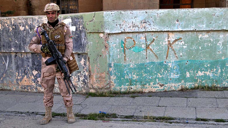 An Iraqi soldier stands guard in Sinjar (Shingal), in front of a wall with PKK-themed graffiti. (Photo: AP)