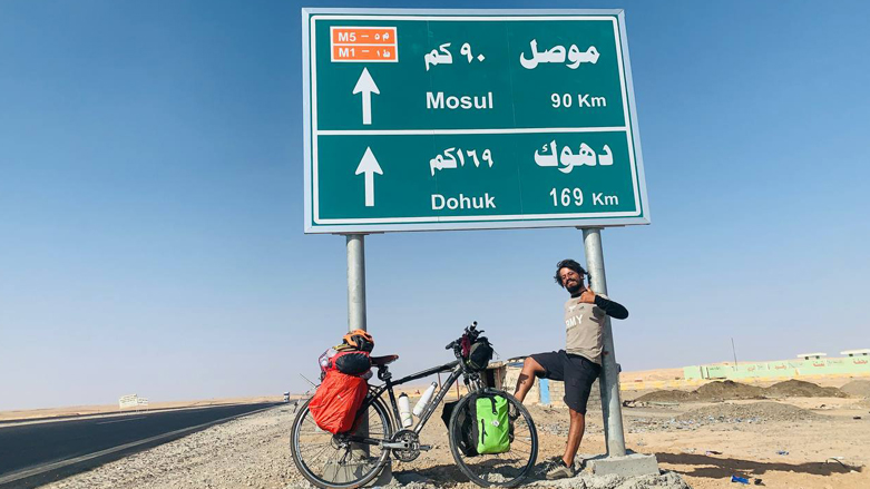 Shaban Sherzad, Kurdish cyclist, poses for a photo under a road sign, Oct. 24, 2022. (Photo: Courtesy of Shaban Sherzad)