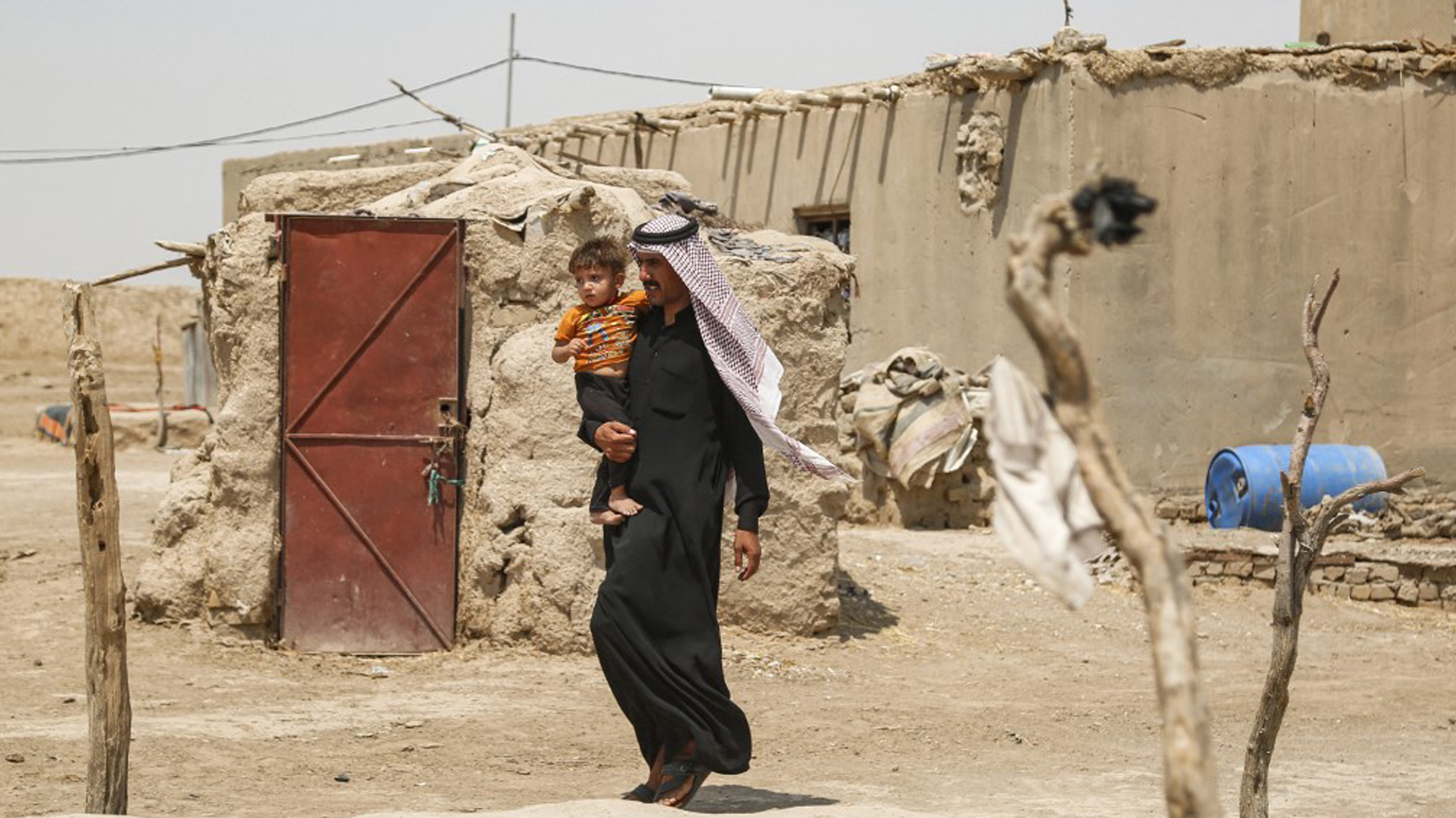 Najeh Farhan carries his son Ali, who is suffering from jaundice, past their mud brick home in the village of al-Zawiyah, in the province of al-Diwayinah, southern Iraq, Aug. 9, 2023. (Photo: Hayder Indhar/AFP)