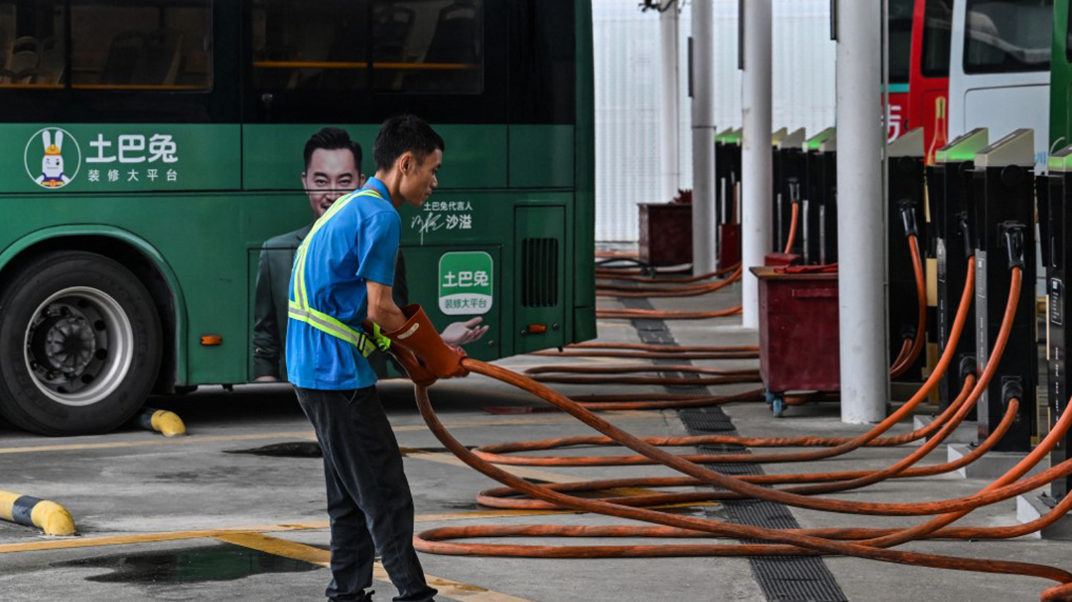 a worker holds a charging cable next to electric buses at Antuoshan charging station in Shenzhen, China's southern Guangdong province, Oct. 18, 2023. (Photo: Hector Retamal/AFP)