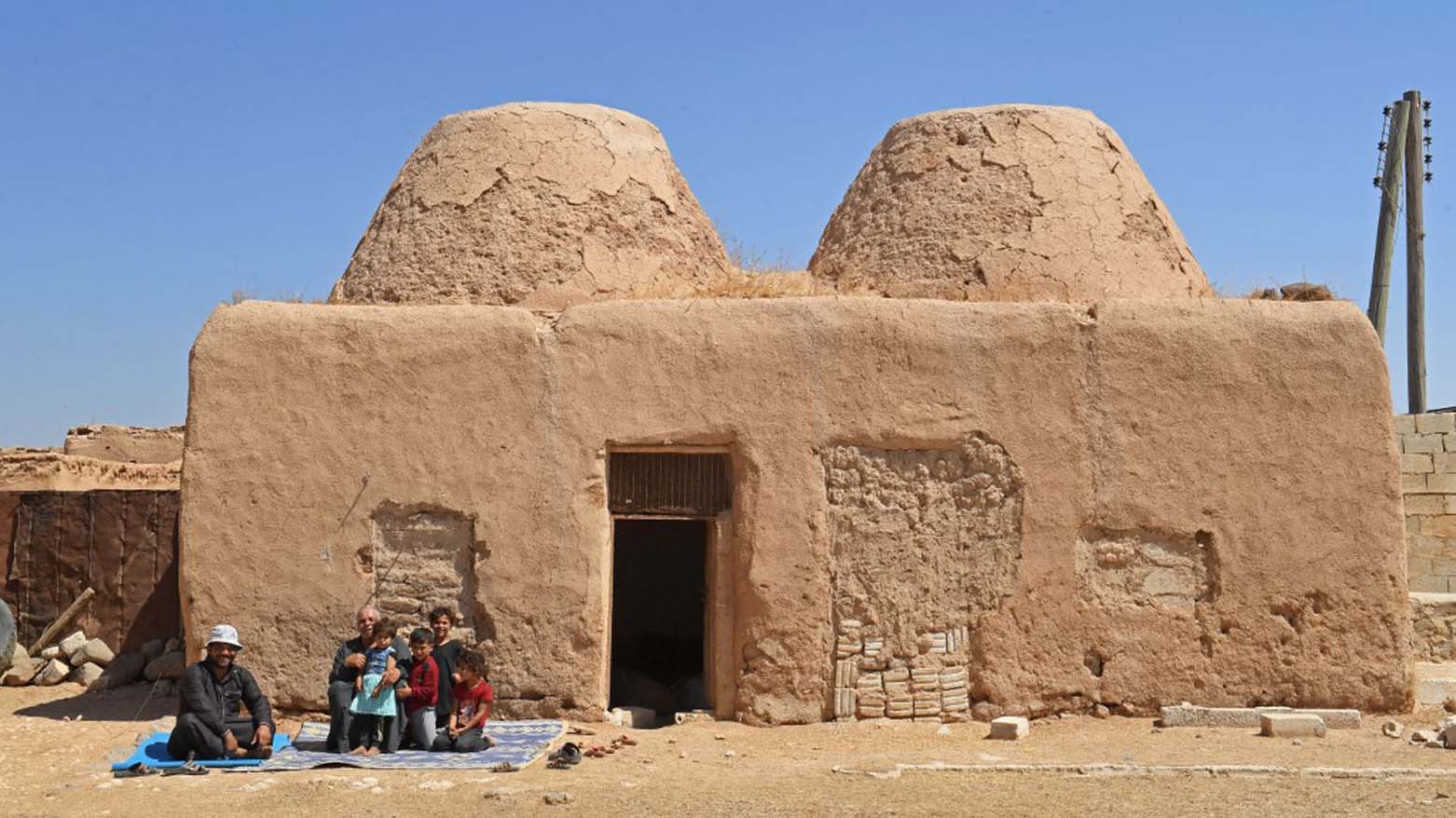 A family sits outside their traditional mud-brick house, known as 'beehive house', in the village of Aqla in Aleppo's eastern countryside, August 11, 2023. (Photo: AFP)
