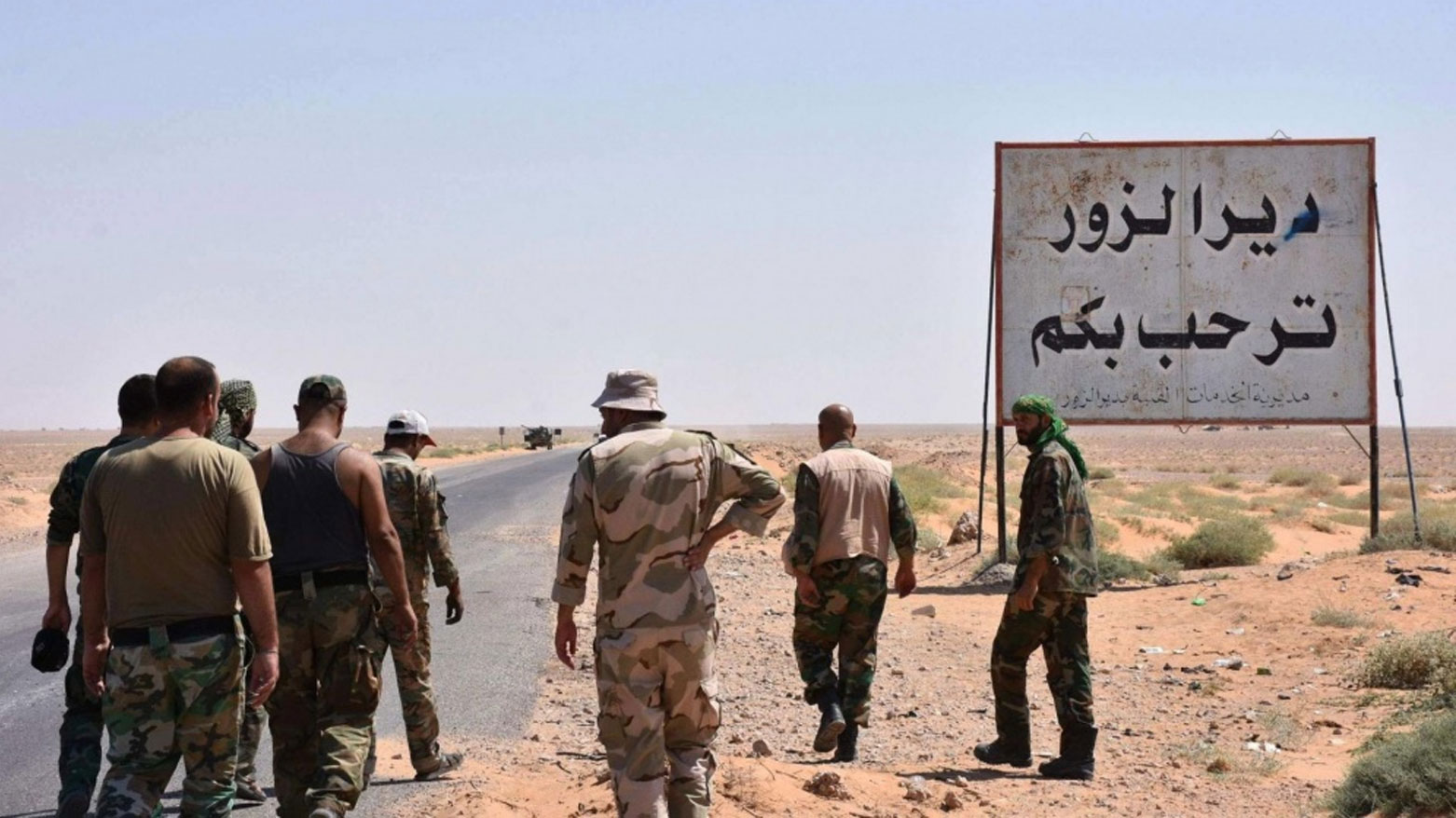 صورة تعبيرية لمجموعة مسلّحين بجانب لوحة تعريفية لمدخل محافظة ديرالزور