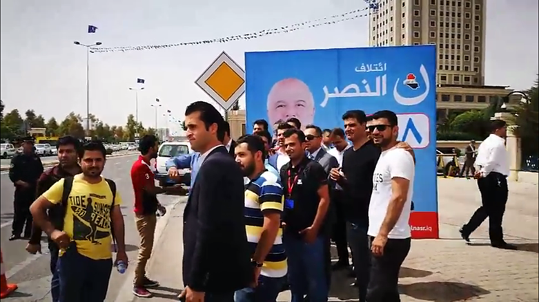 Kurdish journalists standing in front of al-Nasr Coalition billboard after being barred from covering Haider al-Abadi's campaign. 