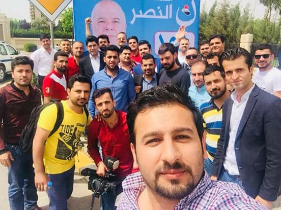Kurdish journalists taking selfie in front of al-Nasr Coalition billboard after being barred from covering Haider al-Abadi's campaign. 