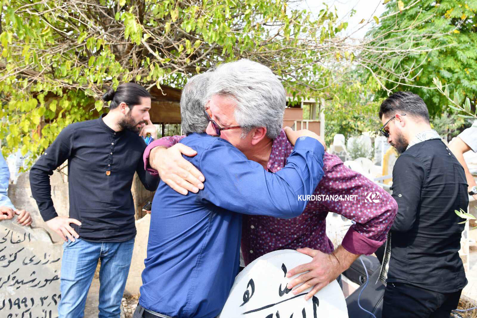 شاعیر و نووسەر ھیوا قادر و ھونەرمەند عەدنان كەریم لەسەر گۆڕی محەمەد عومەر عوسمان باوەش پێكدا دەكەن