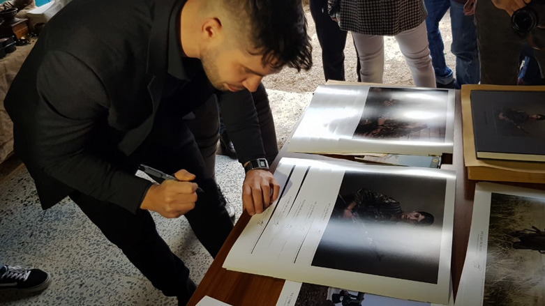 Canadian photographer Joey Lawrence signs copies of his book at in his photo exhibition in the Kurdish city of Sulaimani. (Photo: Kurdistan 24/Wladimir van Wilgenburg)